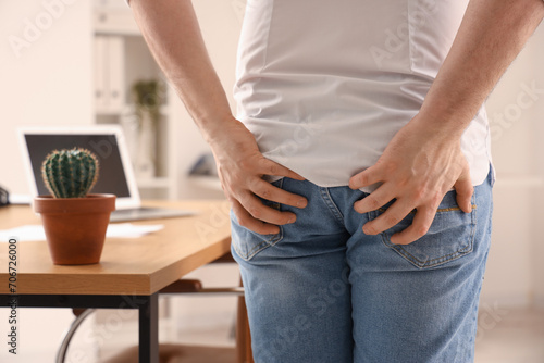 Young businessman with hemorrhoids in office, back view