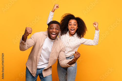Ecstatic black couple celebrating success on a yellow background