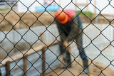 The background is a construction site. Behind the metal mesh fence is a construction site with working people and equipment.