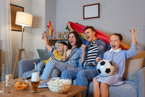 Happy family with Spanish flags watching football game on sofa at home in evening