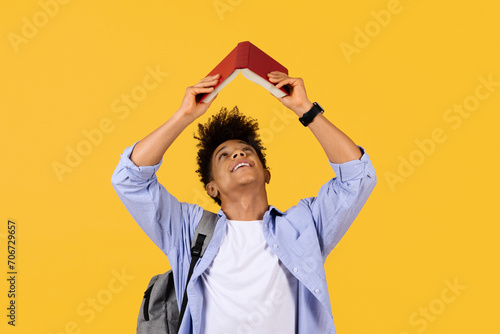 Photos Joyful student with book roof over head on yellow background