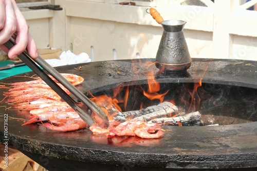 Seafood slices are cooked on a fire pit surface in the shape of cone shaped bowl. Bowl-shaped flat grill with prawns and shrimps. Outdoor barbecue cooking. Street food concept. Toast the hot grilled photo