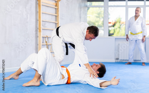 Adult man and young man in kimonos train judo techniques in studio