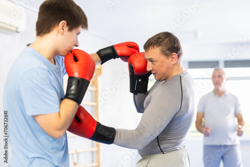 Young boxer in sportswear doing boxing sparring with a trainer in the gym © JackF