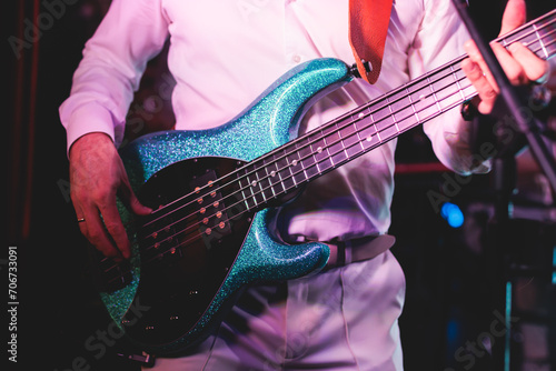 Concert view of a musician, electric bass guitar player with during band performing rock music, bassist player on stage