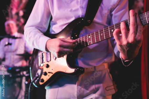 Concert view of an electric guitar player with vocalist and rock band performing in a club, male musician guitarist on stage with audience in a crowded concert hall arena