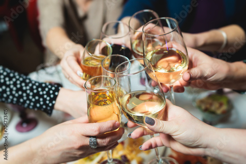 Group of guests celebrate and raise glasses, toasting and cheering with alcohol glasses with wine and champagne in the restaurant on corporate christmas birthday party event or wedding celebration