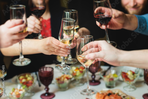 Group of guests celebrate and raise glasses  toasting and cheering with alcohol glasses with wine and champagne in the restaurant on corporate christmas birthday party event or wedding celebration