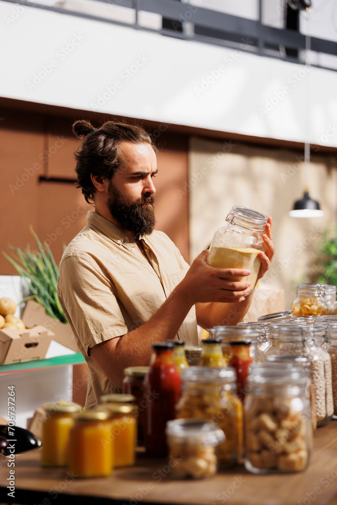 Man in zero waste store taking time to analyze bulk products, making sure they are organic. Customer thoroughly checking food items are environmentally friendly in local neighborhood shop