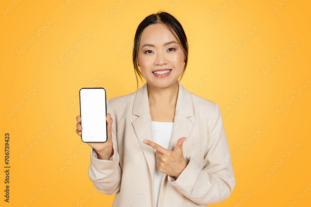 Glad chinese millennial woman in suit, point finger at phone with blank screen, enjoy sale Glad chinese millennial woman in suit, point finger at phone with blank screen, enjoy sale