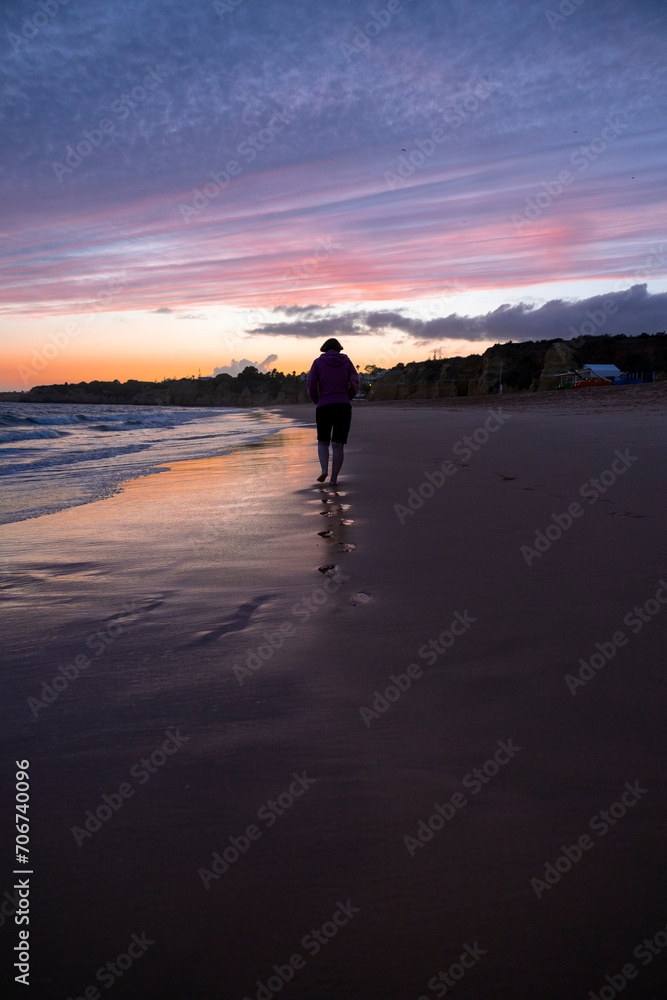Naklejka premium Woman walking on the beach at sunset in the Algarve, Portugal.