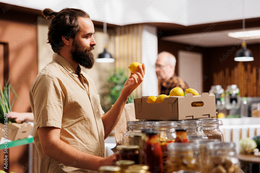 Man in zero waste store taking time to analyze fruits, making sure they are handpicked and farm grown. Green living customer thoroughly checking local supermarket food items are ethically sourced