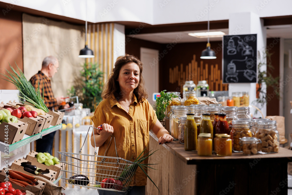 Portrait of cheerful woman looking for locally grown vegetables in eco friendly zero waste store. Hipster client doing grocery shopping, buying organic vegan food items in local neighborhood store Portrait of cheerful woman looking for locally grown vegetables in eco friendly zero waste store. Hipster client doing grocery shopping, buying organic vegan food items in local neighborhood store