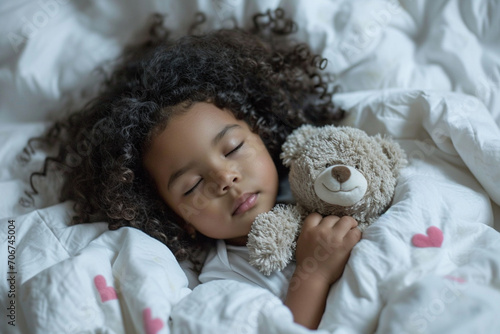 A charming black little girl with curly hair sleeps serenely, gently hugging a soft teddy bear, the concept of sleep and rest, healthy lifestyle and development photo