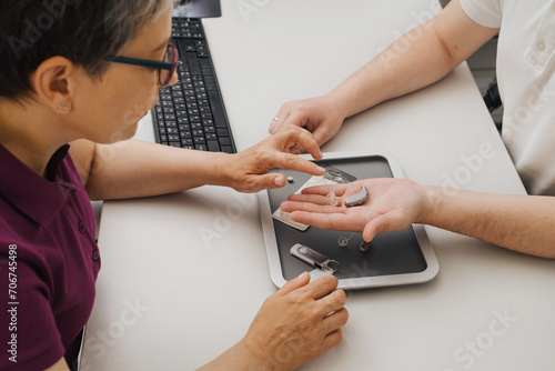 Modern miniature hearing aids. Small and discreet invisible hearing aids in hands. Closeup of patient and doctor. Hearing rehabilitation clinic