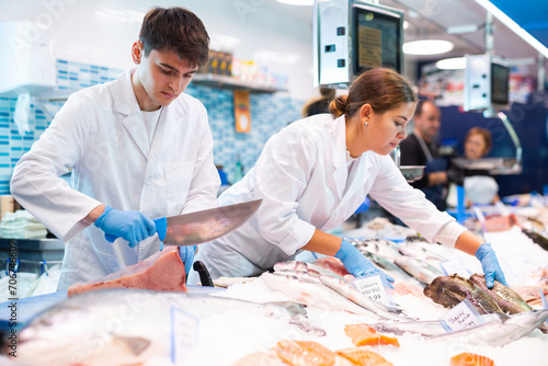 Proficient sellers in white work clothes processing tuna on table board in fish shop photo
