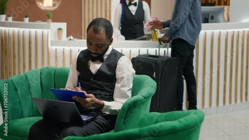 Tourism industry employee. Bellboy entering data document forms on papers in lounge area, hotel concierge making entry in daily luggage movement register, using clipboard notes. photo