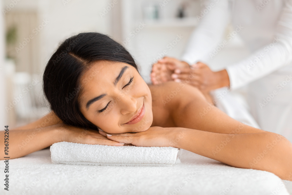 Joyful young indian woman receiving relaxing back massage Joyful young indian woman receiving relaxing back massage