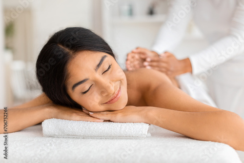 Joyful young indian woman receiving relaxing back massage