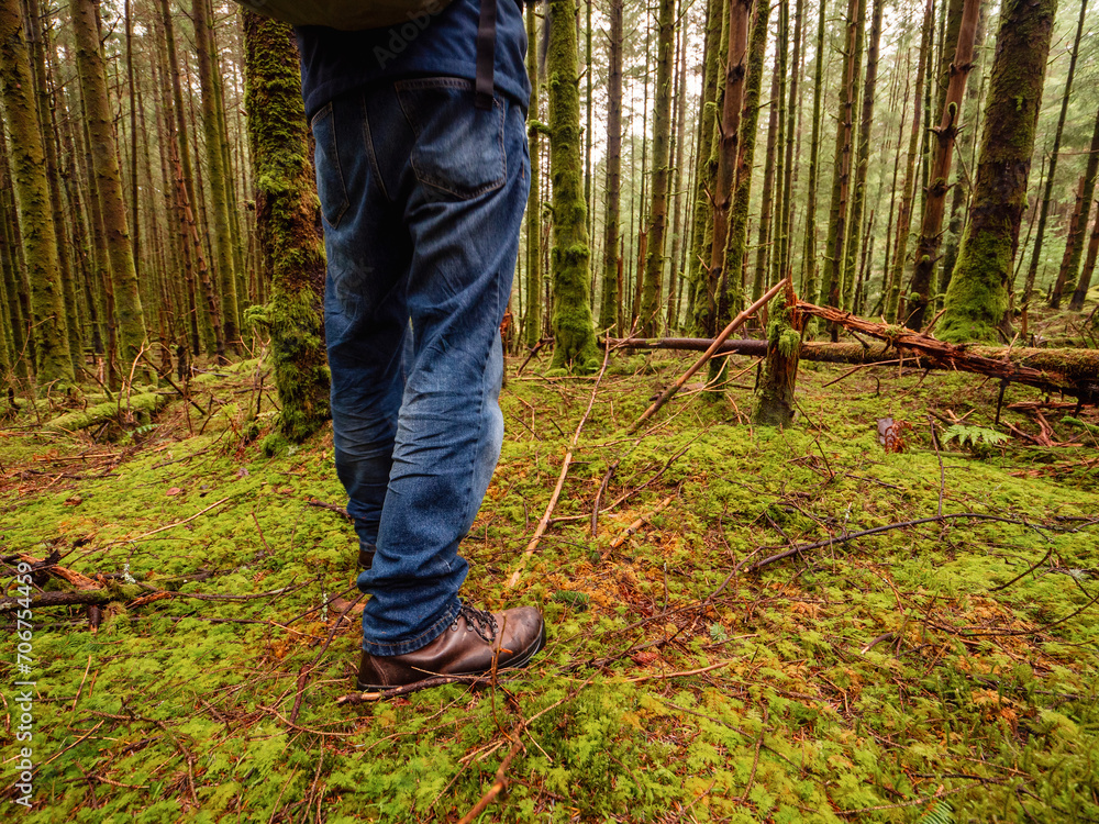 Tourist in blue jeans and tough brown leather outdoor boots on a green moss in a dense forest. Trip to nature and outdoor activity concept. Tourist in blue jeans and tough brown leather outdoor boots on a green moss in a dense forest. Trip to nature and outdoor activity concept.