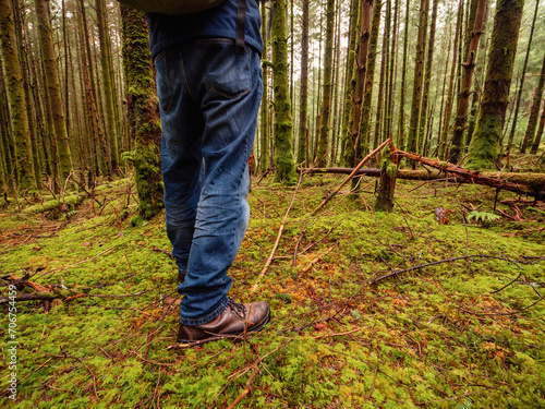 Tourist in blue jeans and tough brown leather outdoor boots on a green moss in a dense forest. Trip to nature and outdoor activity concept.