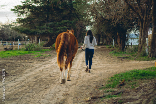 woman walking in a field next to a brown horse