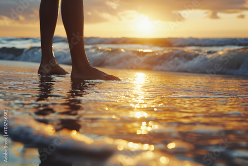 Standing at the Shoreline During Sunset. Close-up of a man's legs standing on the shore, with the sun setting over the ocean horizon and reflections in the water. Horizontal photo