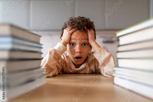 Stressed black boy surrounded by towering stacks of books photo