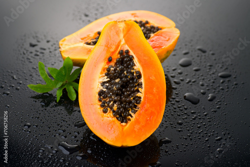 Papaya fruit on wet black background with water drops. Halved fresh organic Papaya exotic fruits with leaf close up. Healthy vegan food. 