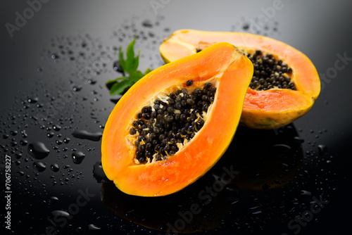 Papaya fruit on wet black background with water drops. Halved fresh organic Papaya exotic fruits with leaf close up. Healthy vegan food