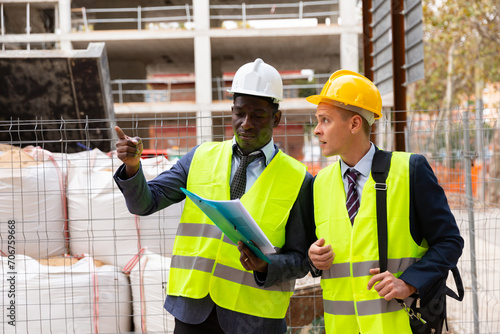 Portrait of two engineers in helmet and yellow vests. Indicate finger to the side