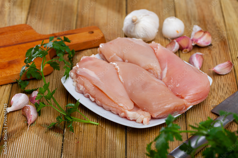 Raw boneless chicken breast on wooden surface with seasonings. Dietary cooking ingredient
