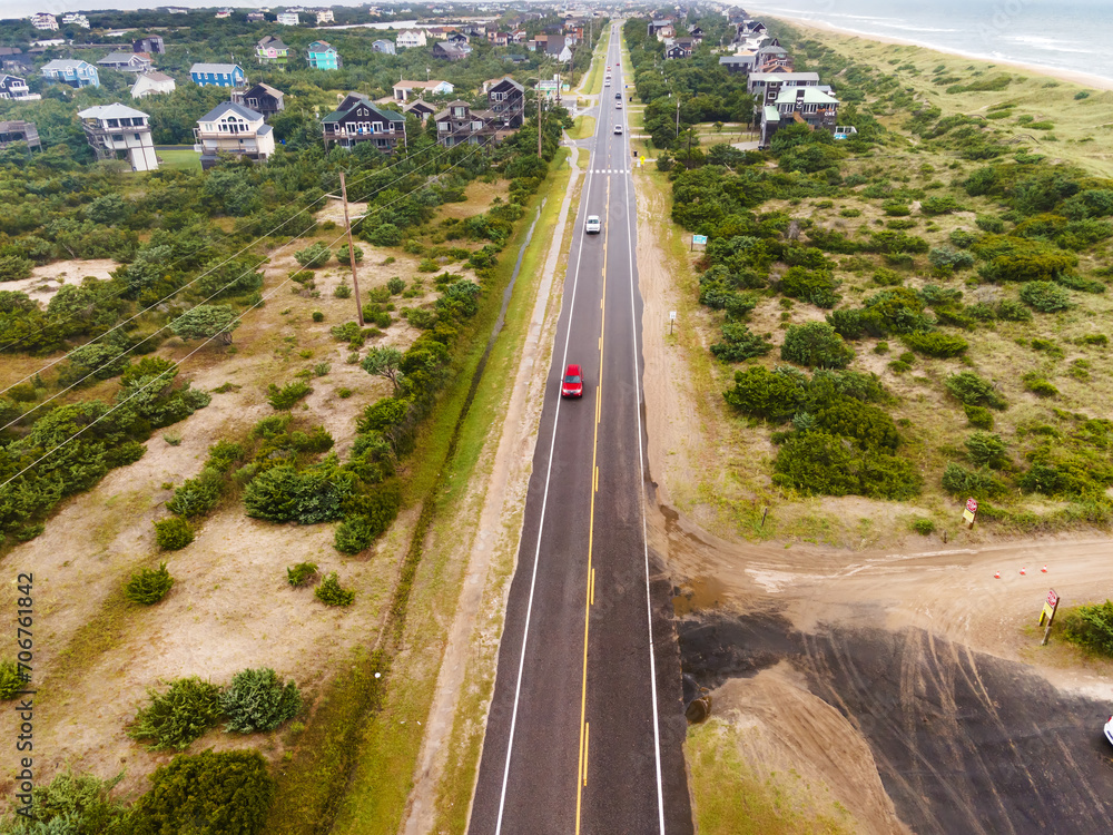 road through a small town in America along the ocean filmed from a drone. Houses, trees, cars.