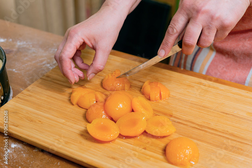 Woman cutting apricots at wooden board in kitchen, closeup. Preparing the pie filling.