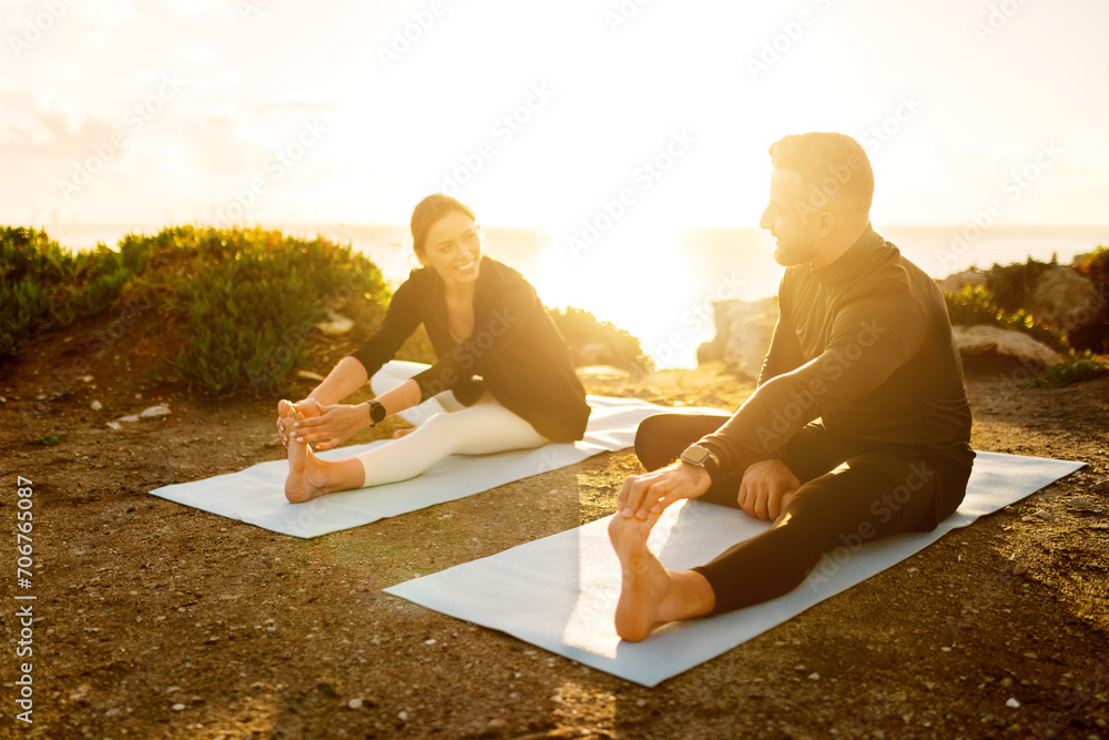 Fototapeta premium Couple sharing laugh while doing yoga stretches seaside