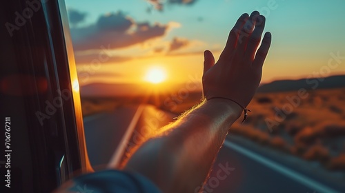Road trip concept - hand held out of an open window, sunset in the foreground