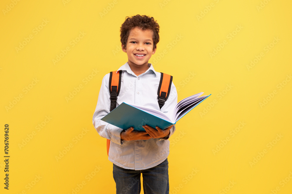 Schoolboy reading book with backpack on yellow background Schoolboy reading book with backpack on yellow background