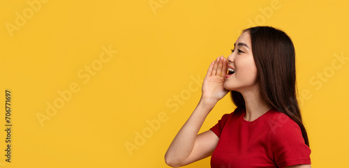 Young asian woman screaming towards copy space, yellow background
