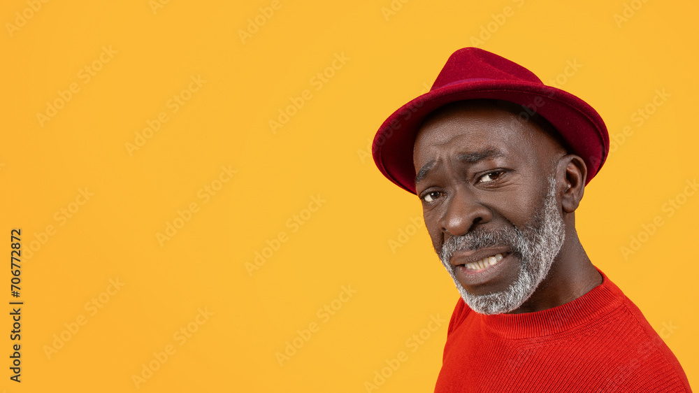 Skeptical black senior man with a questioning expression, wearing a red sweater and hat