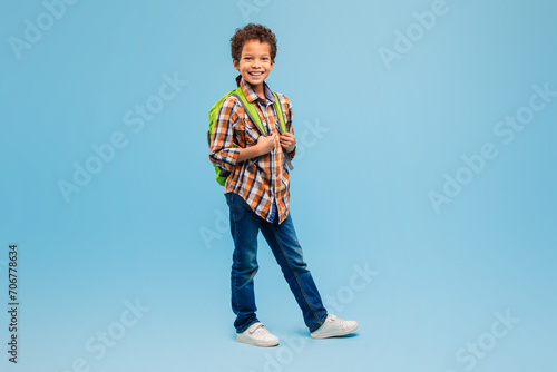 Smiling boy with backpack in plaid shirt, blue background