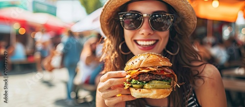 stylish hipster woman holding juicy burger and eating boho girl biting hamburger smiling at street food festival summertime summer vacation travel space for text. with copy space image