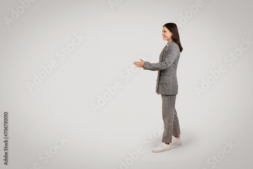 Side view of woman in suit extending hand, grey background