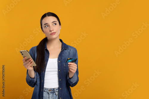 Confused woman with credit card and smartphone on orange background, space for text. Debt problem