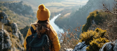 Traveler millennial girl in yellow beanie hat with backpack sitting on cliff edge with autumn forest and enjoying beautiful valley view Adventure vacations. with copy space image photo