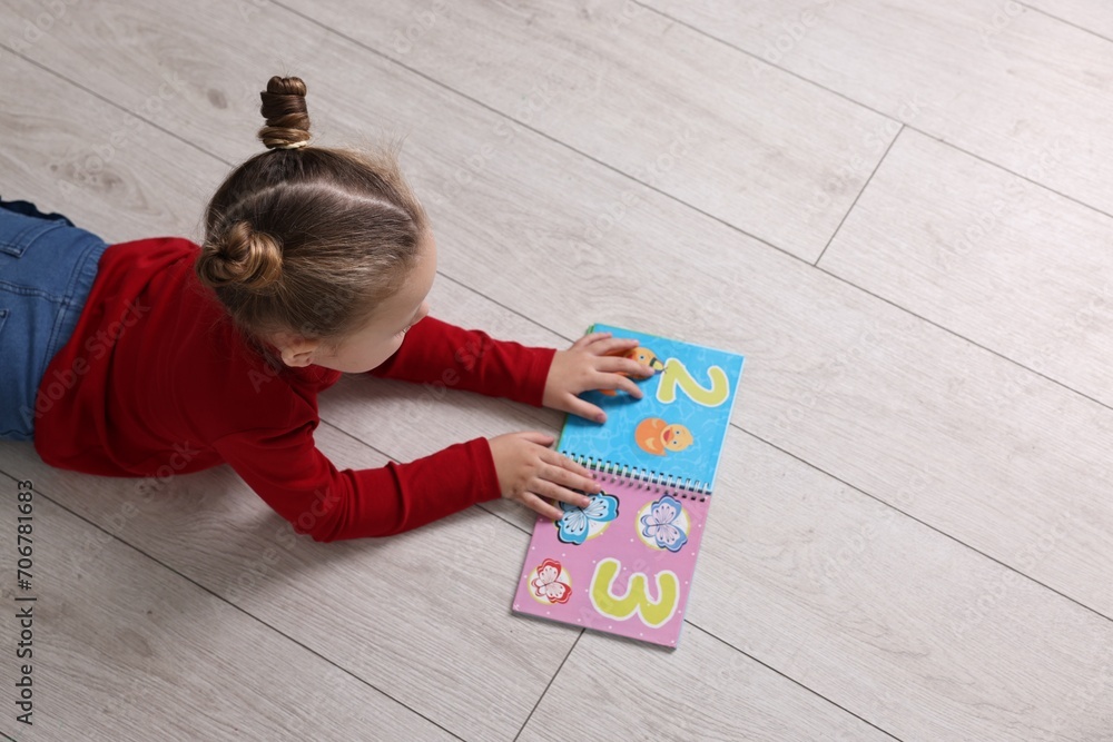 Cute little girl reading book on warm floor indoors, space for text. Heating system Cute little girl reading book on warm floor indoors, space for text. Heating system