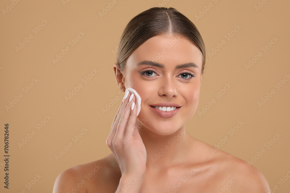 Beautiful woman removing makeup with cotton pad on beige background Beautiful woman removing makeup with cotton pad on beige background