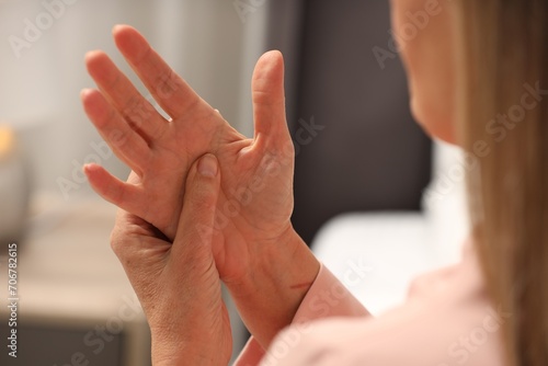 Mature woman suffering from pain in hand indoors, closeup. Rheumatism symptom