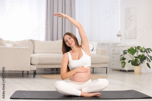 Pregnant woman stretching on yoga mat at home