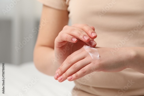 Young woman with dry skin applying cream onto her hand indoors, closeup