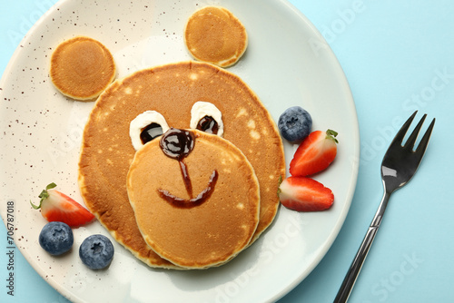 Creative serving for kids. Plate with cute bear made of pancakes and berries on light blue table, flat lay